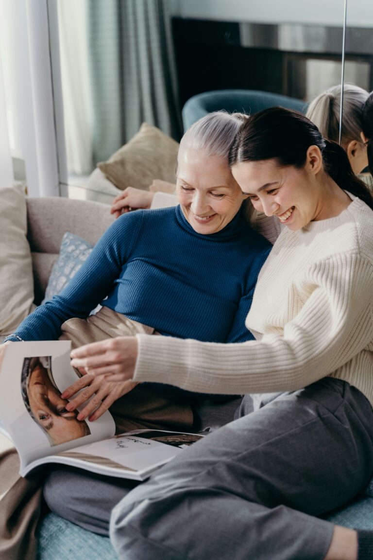 Mom and daughter sitting on a couch, smiling and looking at a magazine together.