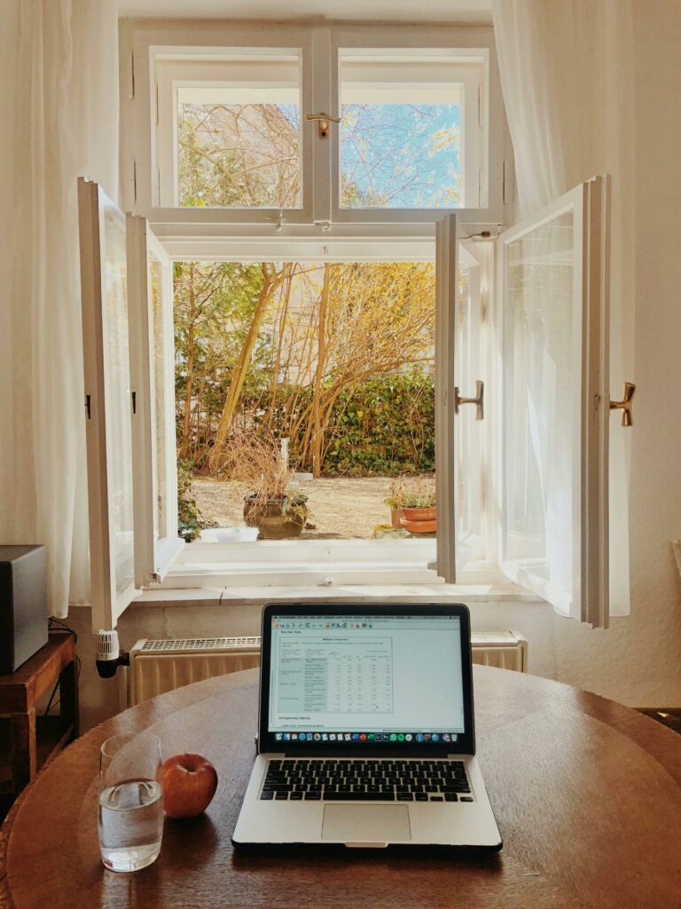 Laptop on wooden table in front of a window.