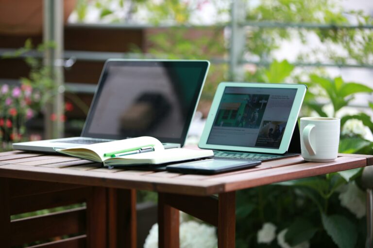 Two laptops and an iPad on a desk behind a notebook