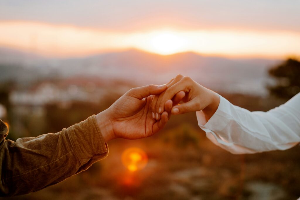 Zoom in people's hands while holding eachother in front of the sunset.