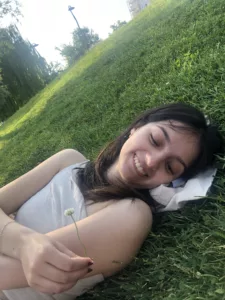 Brunette women laying on the grass smiling, while holding a flower.